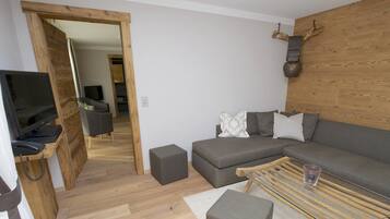 Una sala moderna con un sofá gris, una mesa de centro de cristal y un mueble de televisión de madera.