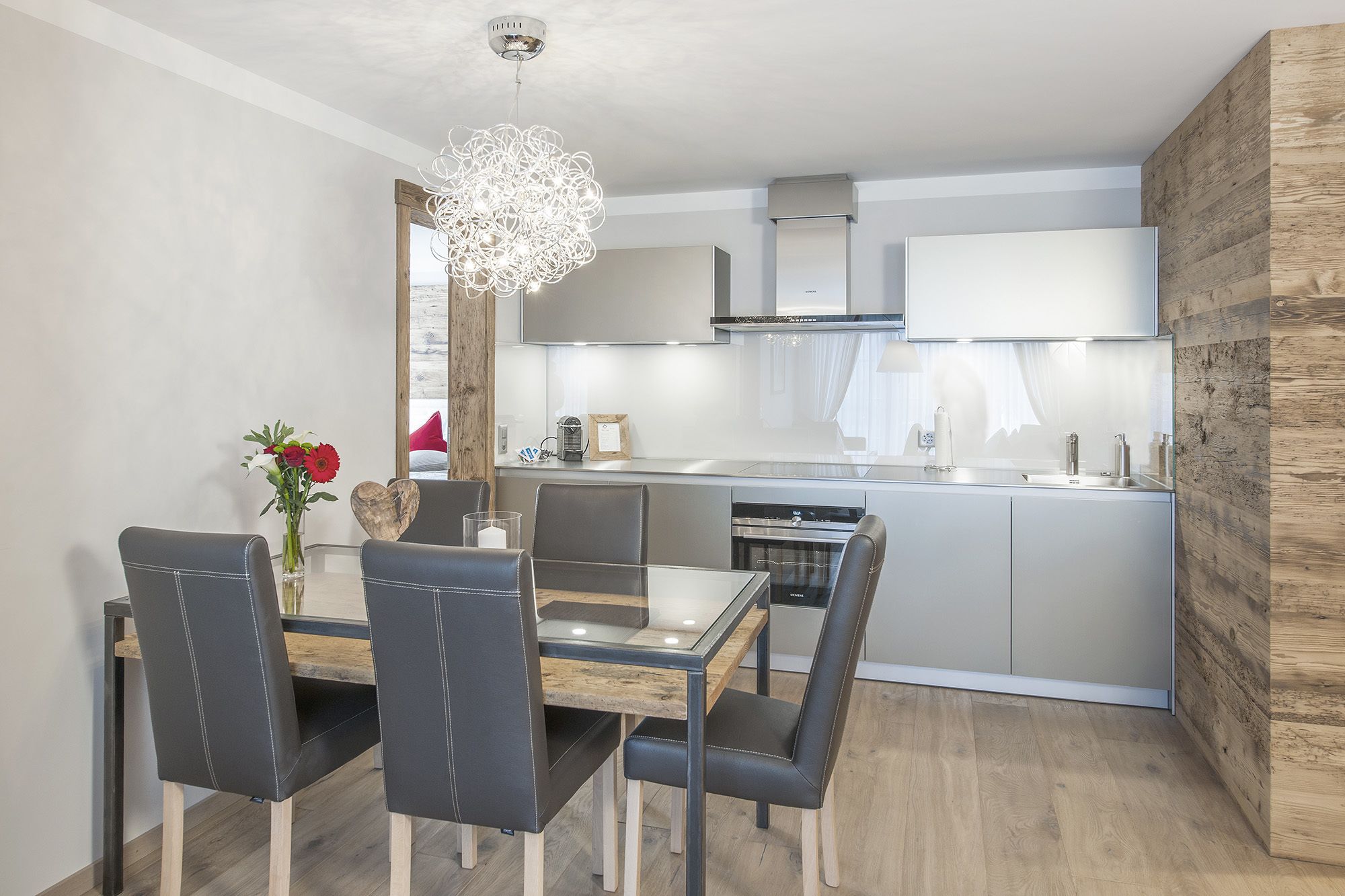 Una cocina moderna con una isla central, electrodomésticos de acero inoxidable y un comedor con mesa de vidrio y sillas de cuero.