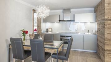 Una cocina moderna con una isla central, electrodomésticos de acero inoxidable y un comedor con mesa de vidrio y sillas de cuero.