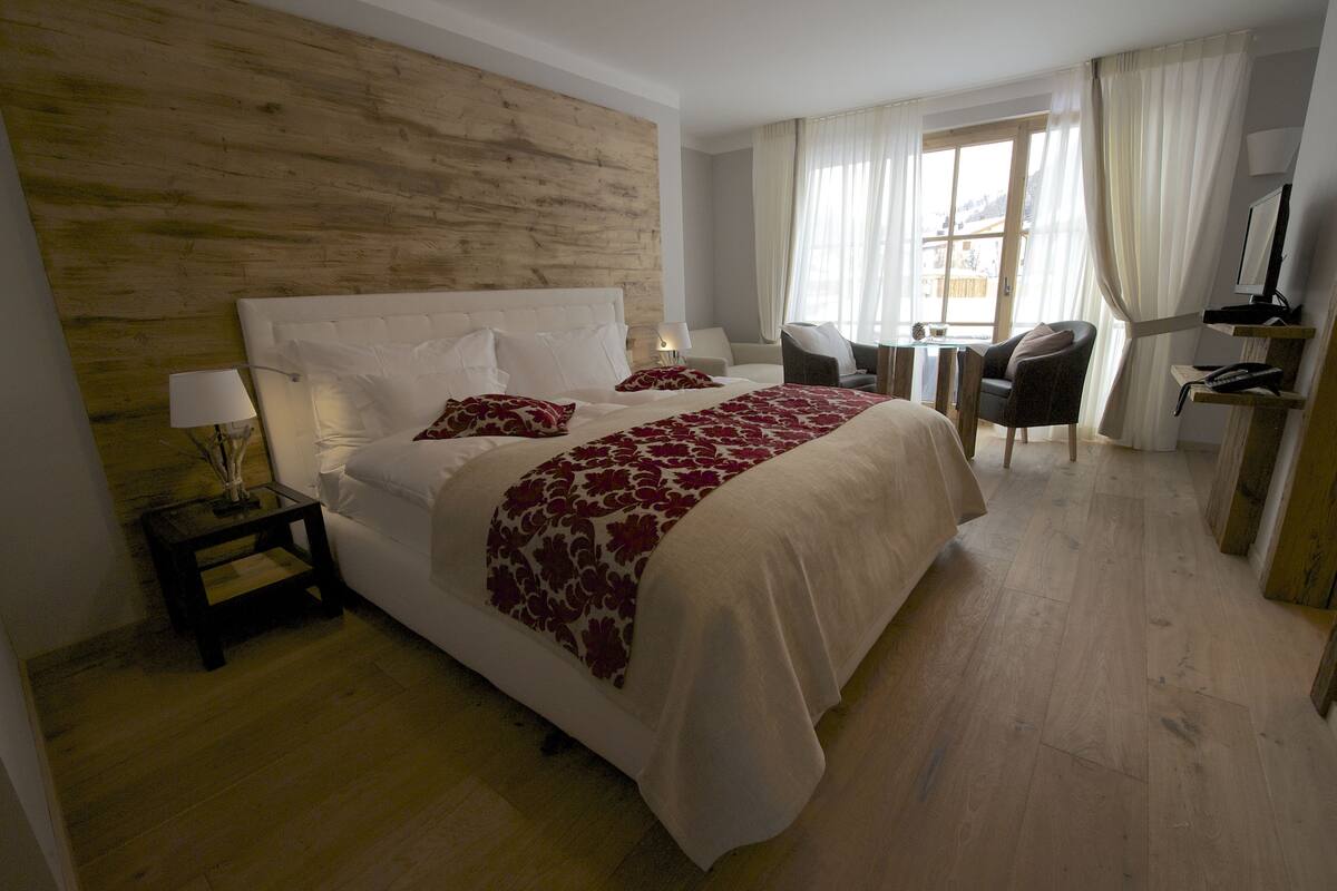 Habitación de hotel con una cama grande, una mesita de noche con lámpara, una silla y un escritorio con computadora y teléfono.
