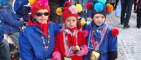 Three children in traditional attire with colorful pom-poms, standing outdoors.