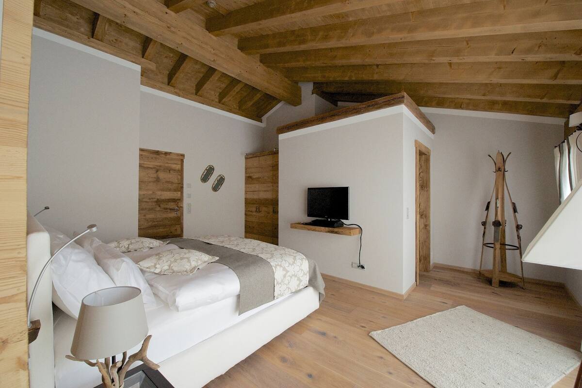 Un dormitorio con una cama, televisor, techo de madera y perchero.