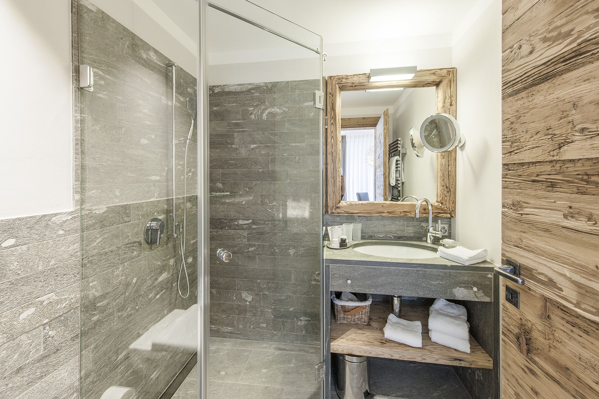 Un baño con ducha de vidrio, lavabo con tocador de madera y espejo con marco de madera.