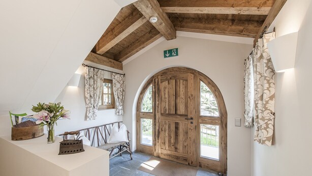 A rustic interior with a wooden door, a bench, and a vase with flowers. - Hotelino Petit Chalet (Celerina-Schlarigna)