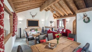 A rustic interior with a wooden dining table, red upholstered sofas, and a fireplace. - Hotelino Petit Chalet (Celerina-Schlarigna)