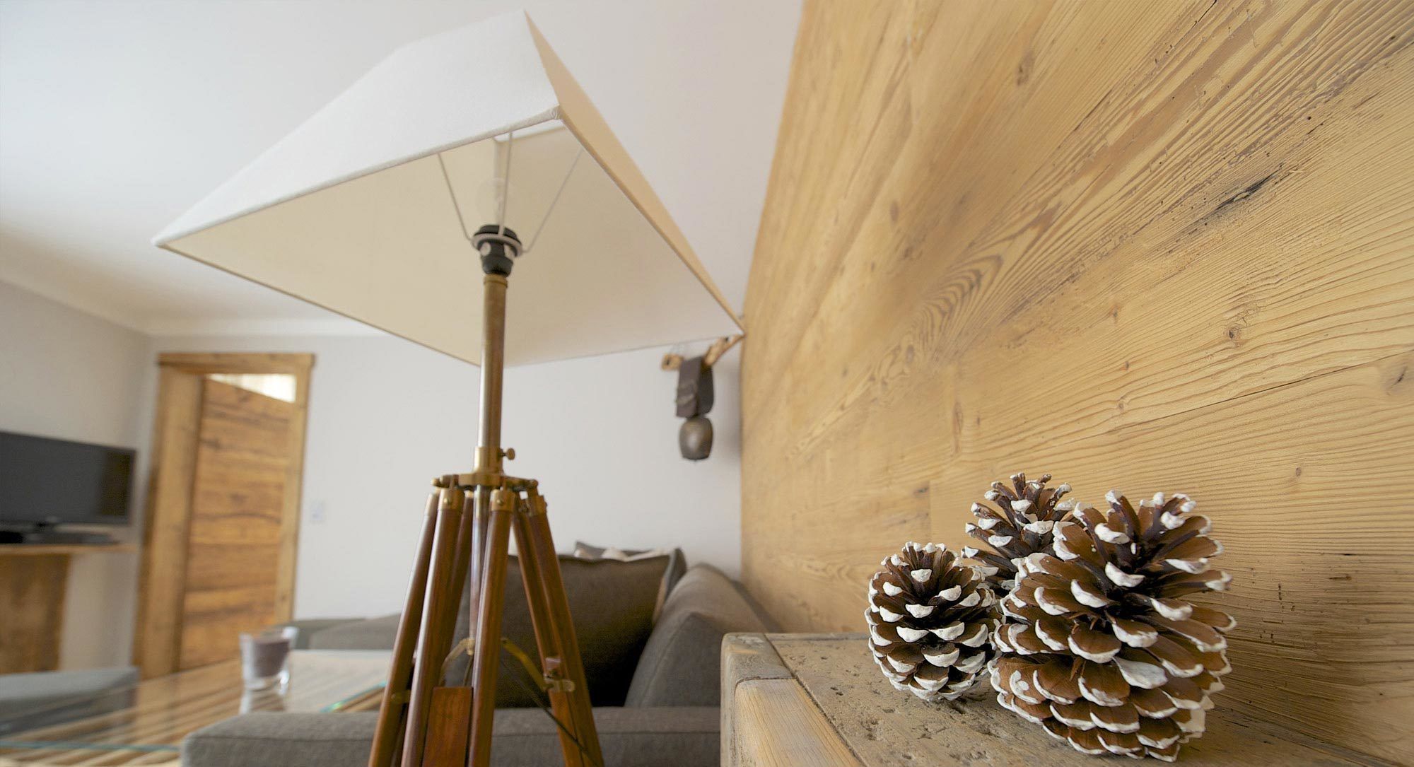 A room with a tripod-mounted floor lamp, a wooden wall, and pine cones on a table.