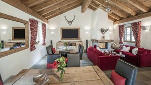 A rustic interior with exposed wooden beams, a fireplace, red upholstered furniture, and a dining area with a wooden table and chairs. - Hotelino Petit Chalet (Celerina-Schlarigna)