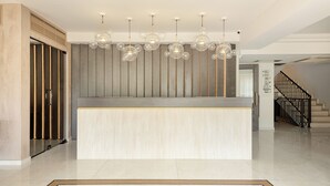A reception area with a modern design, featuring a central counter, a patterned floor, and a staircase in the background. - Corfu Mare Hotel (Corfu)