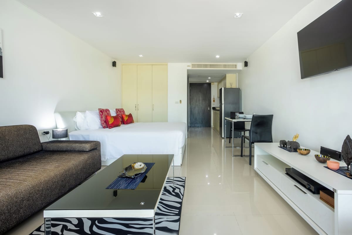 A modern hotel room with a bed, sofa, TV, and a dining area.