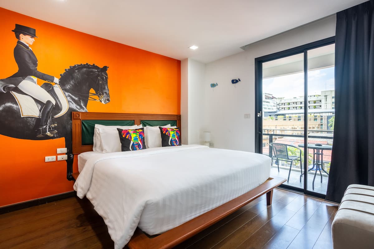 A hotel room with a large bed, a balcony with a view of buildings, and a mural of a horse rider on the wall.