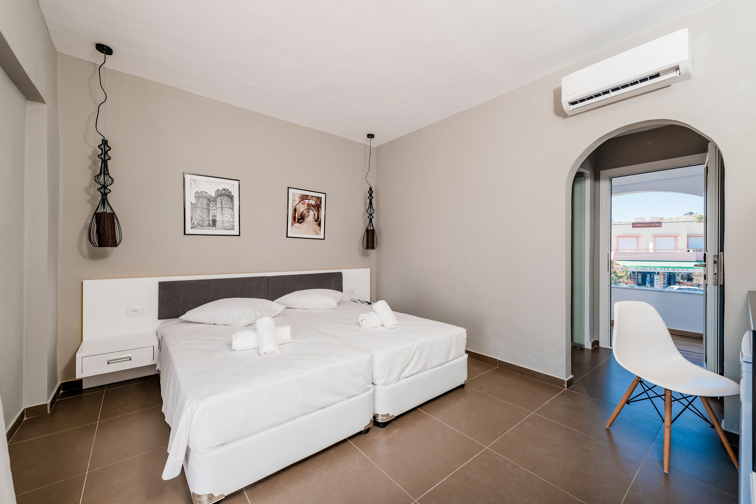 Quarto de hotel moderno com cama de casal, mesa de cabeceira, uma cadeira e duas obras de arte penduradas na parede.