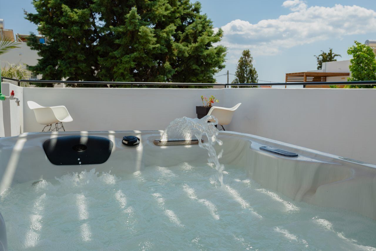 A hot tub with water jets, two white chairs, and a potted plant.