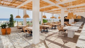 An outdoor dining area with tables and chairs, a thatched roof, and a view of the sea. - Belmare Hotel (Rhodes)