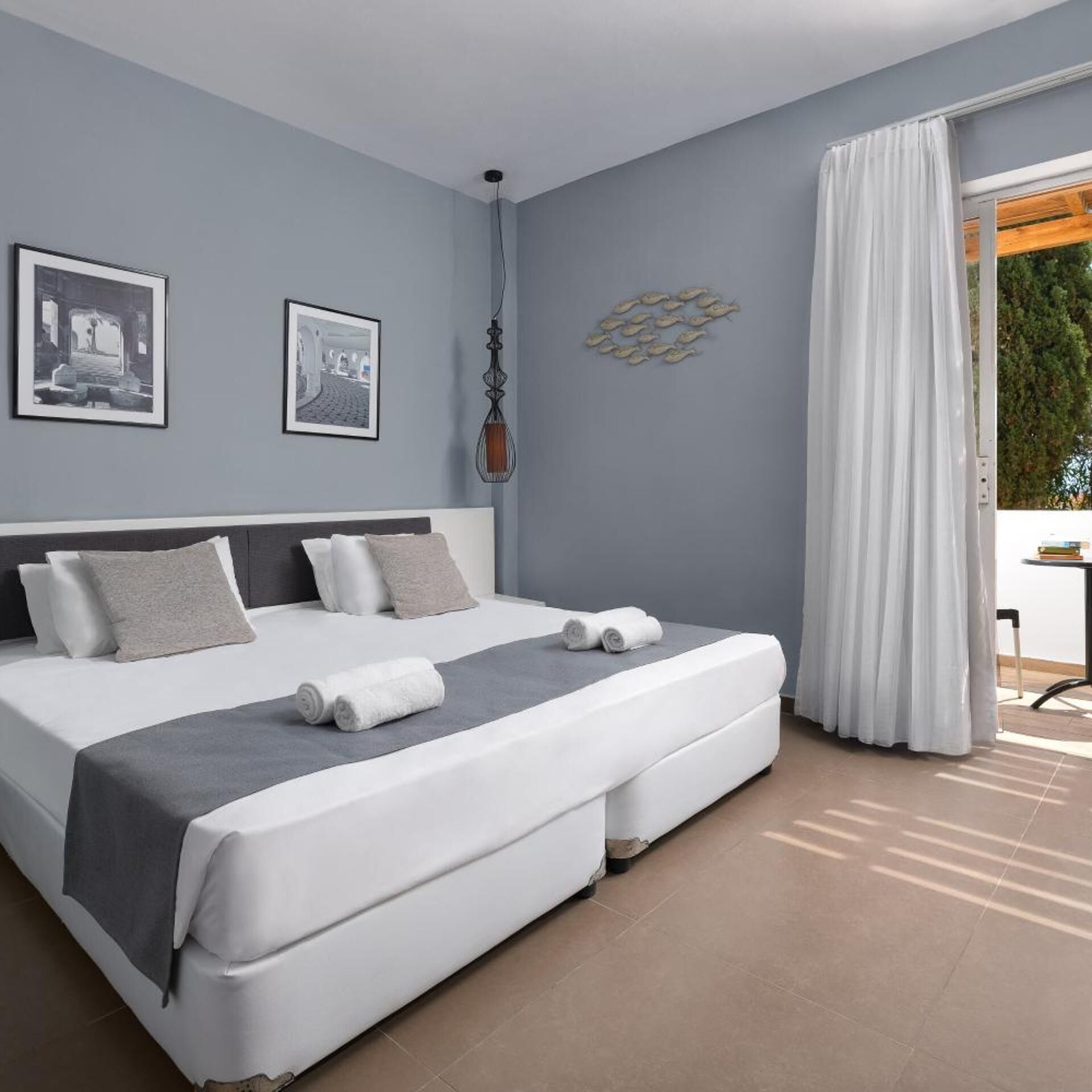 Quarto moderno com cama grande, duas almofadas, mesa de cabeceira e vista para o exterior.