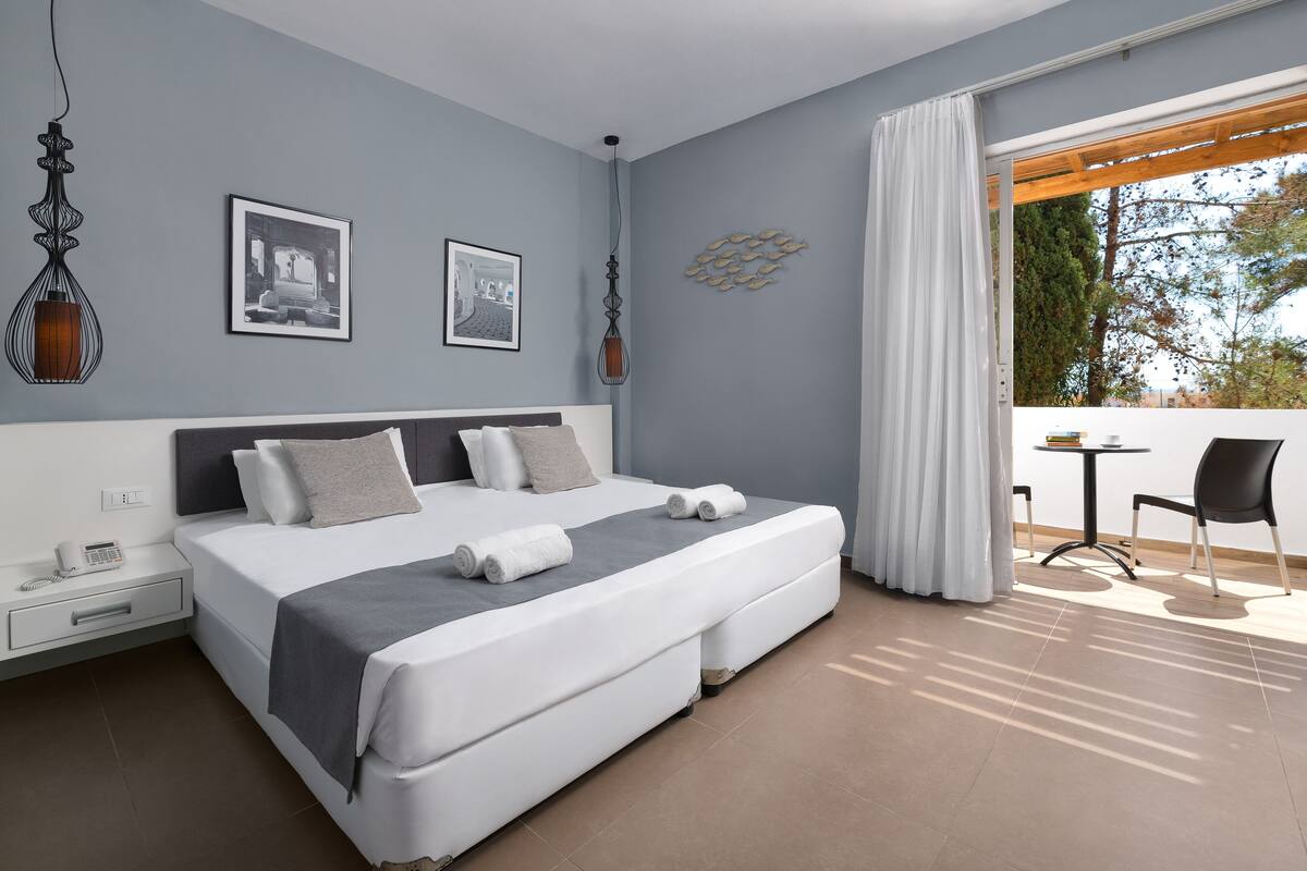 A modern hotel room with a large bed, a small table, and a balcony with a view.