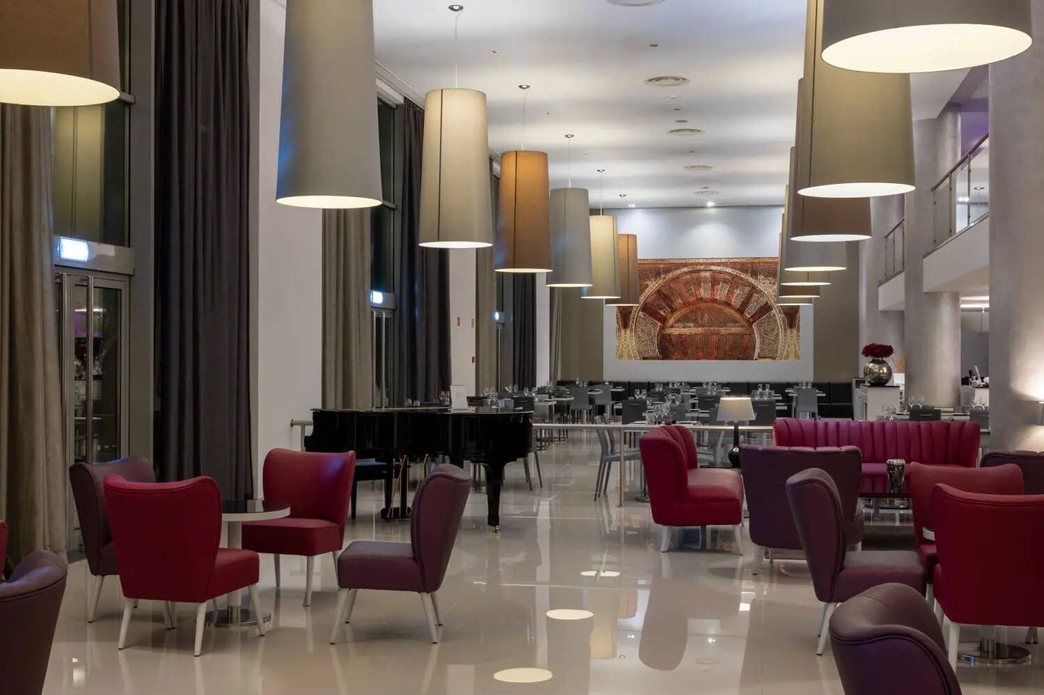 A spacious lobby with modern red chairs, a grand piano, and large pendant lights.