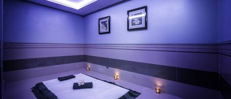 Een spa ruimte met een witte massagetafel, handdoeken en kaarsen.