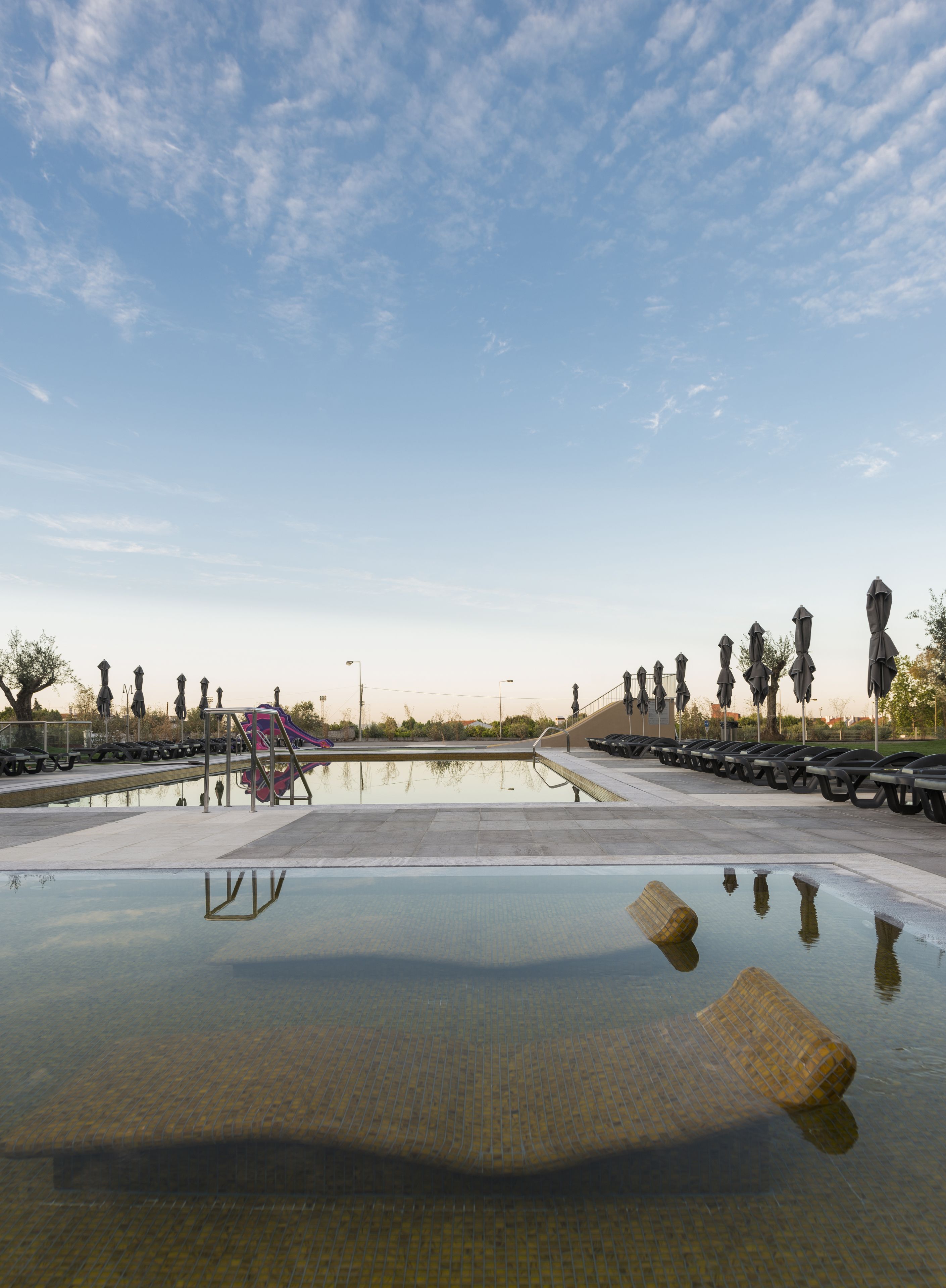 Une piscine avec un toboggan, entourée de parasols et de bancs.