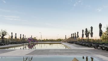 Une piscine avec un toboggan, entourée de parasols et de bancs.