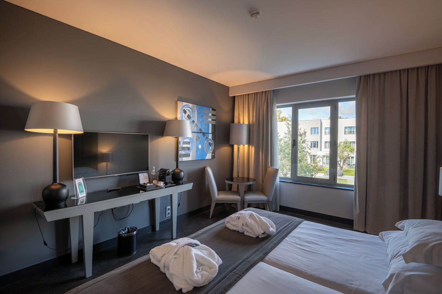 Habitación de hotel con cama, escritorio, silla y un ventanal grande.