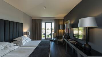 Habitación de hotel moderna con una cama grande, un escritorio con lámpara, una silla y vistas al exterior.