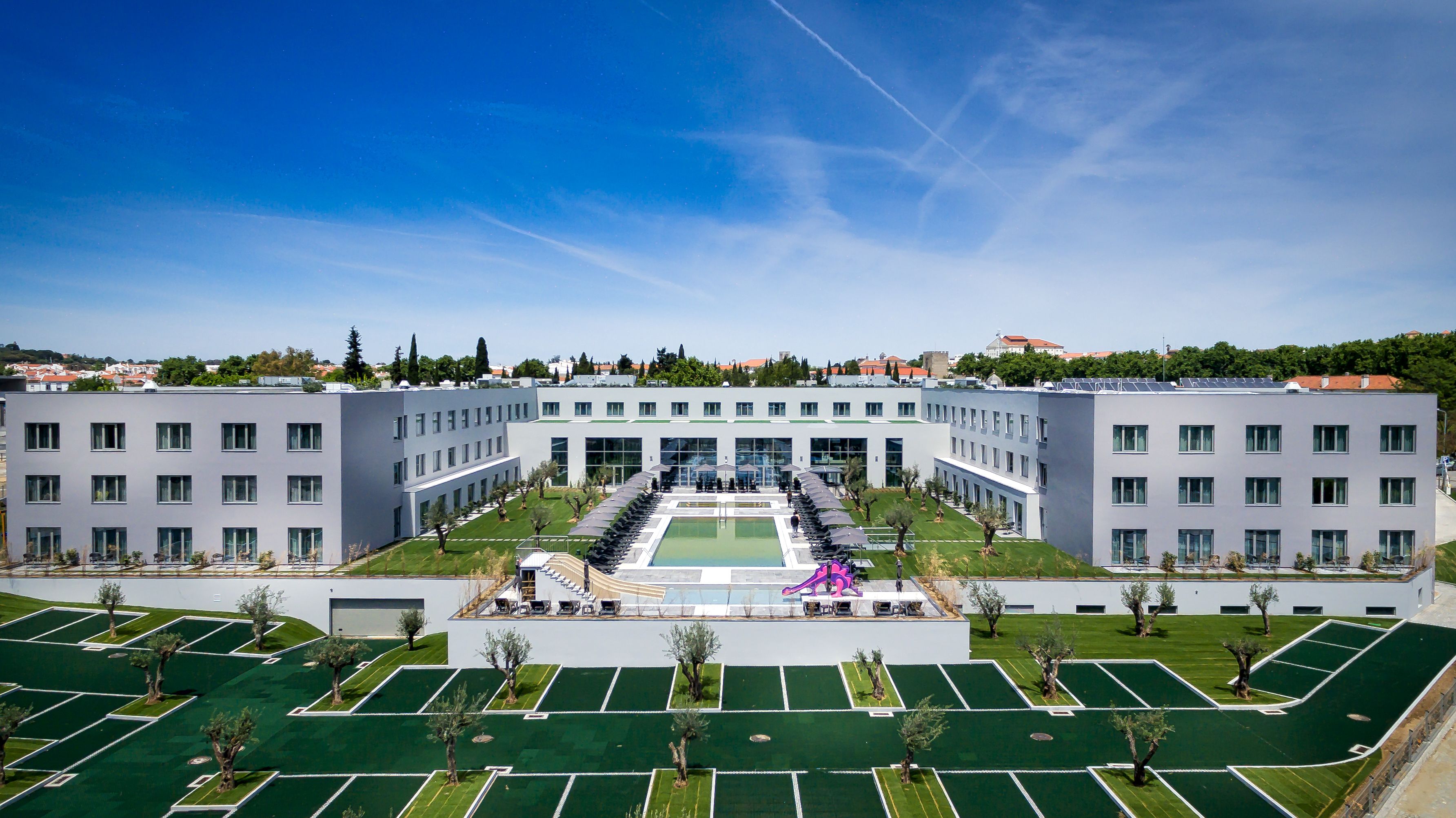 A modern building with a central courtyard, multiple floors, and a parking area with green spaces.