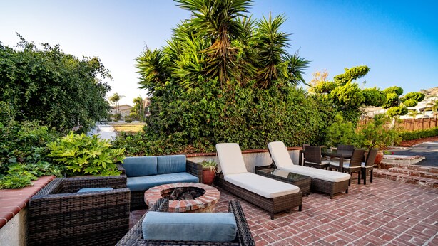 A patio with wicker furniture, a fire pit, and lush greenery.