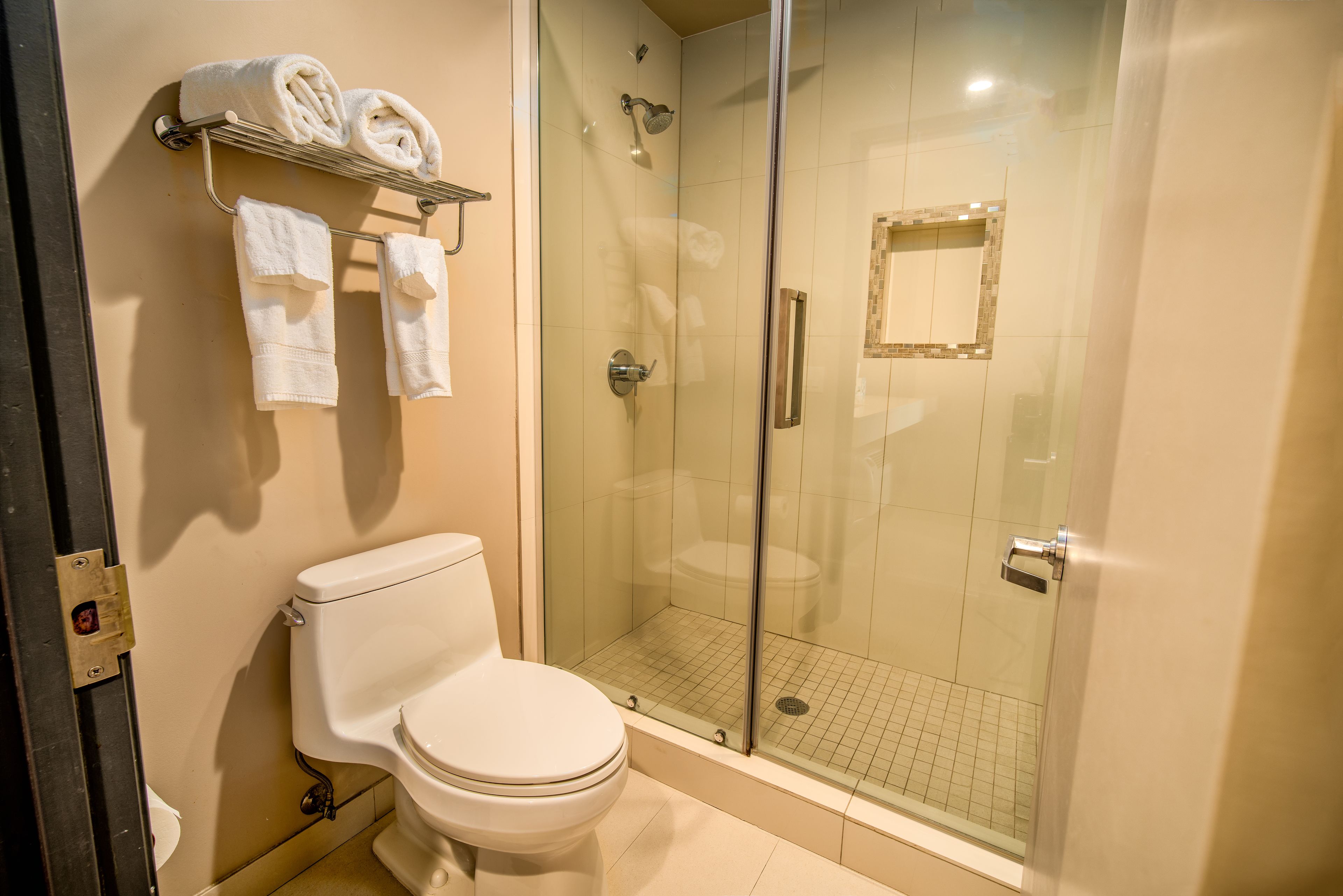 Un baño con inodoro, ducha con cerramiento de vidrio y toallero con toallas.