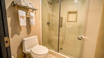 Un baño con inodoro, ducha con cerramiento de vidrio y toallero con toallas.