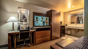 A hotel room with a desk, chair, television, bed, and bathroom.