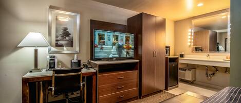 A hotel room with a desk, chair, television, bed, and bathroom.