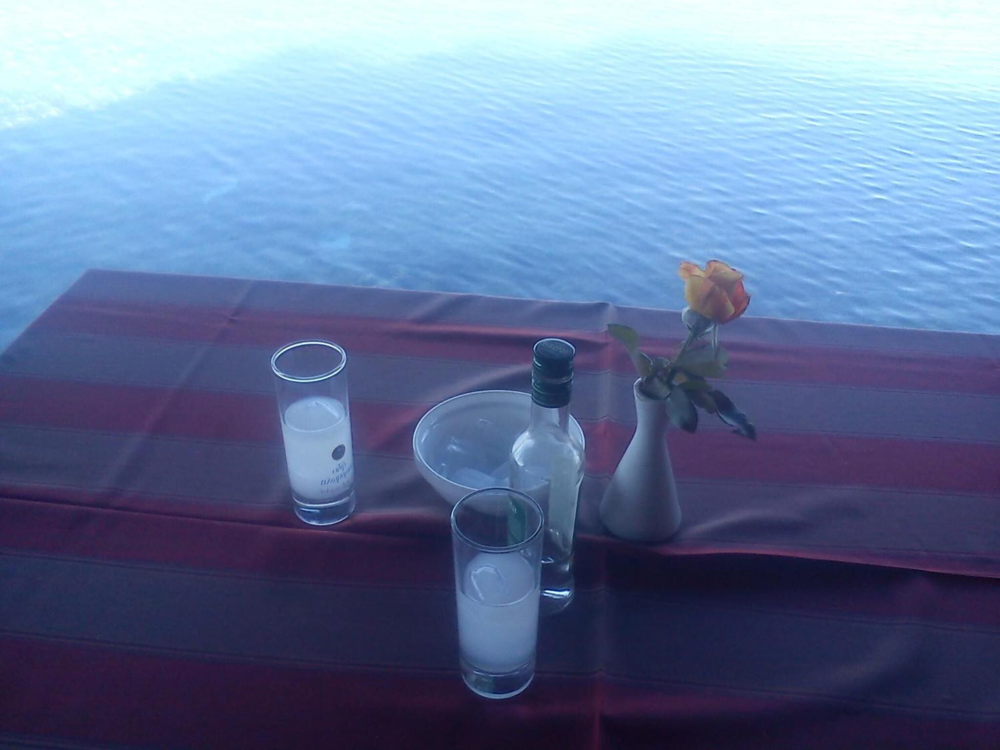 Una mesa con un vaso de agua, una botella y un florero con una rosa.