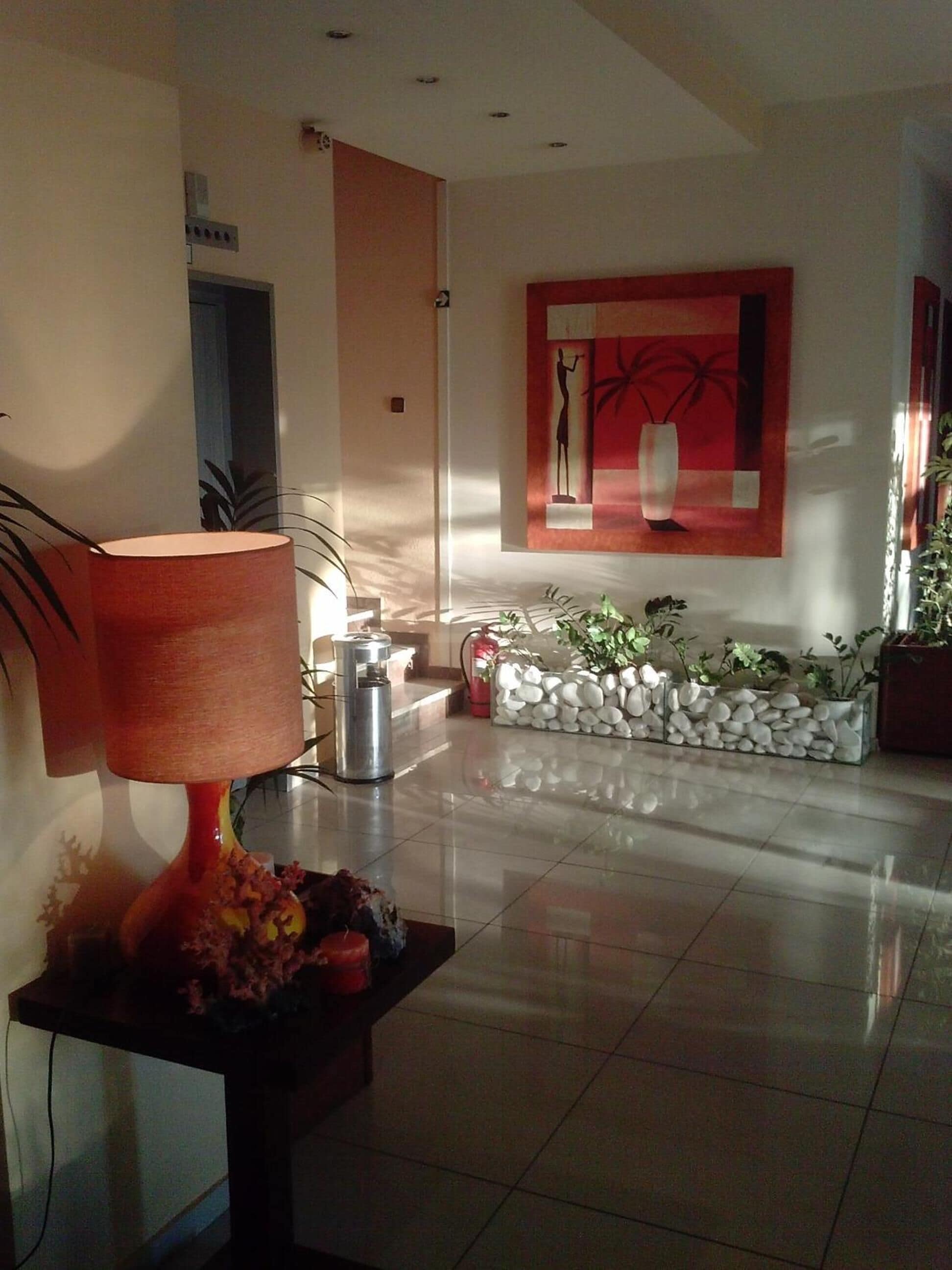 A modern lobby with a tiled floor, a decorative lamp, a stone planter, and a painting on the wall.