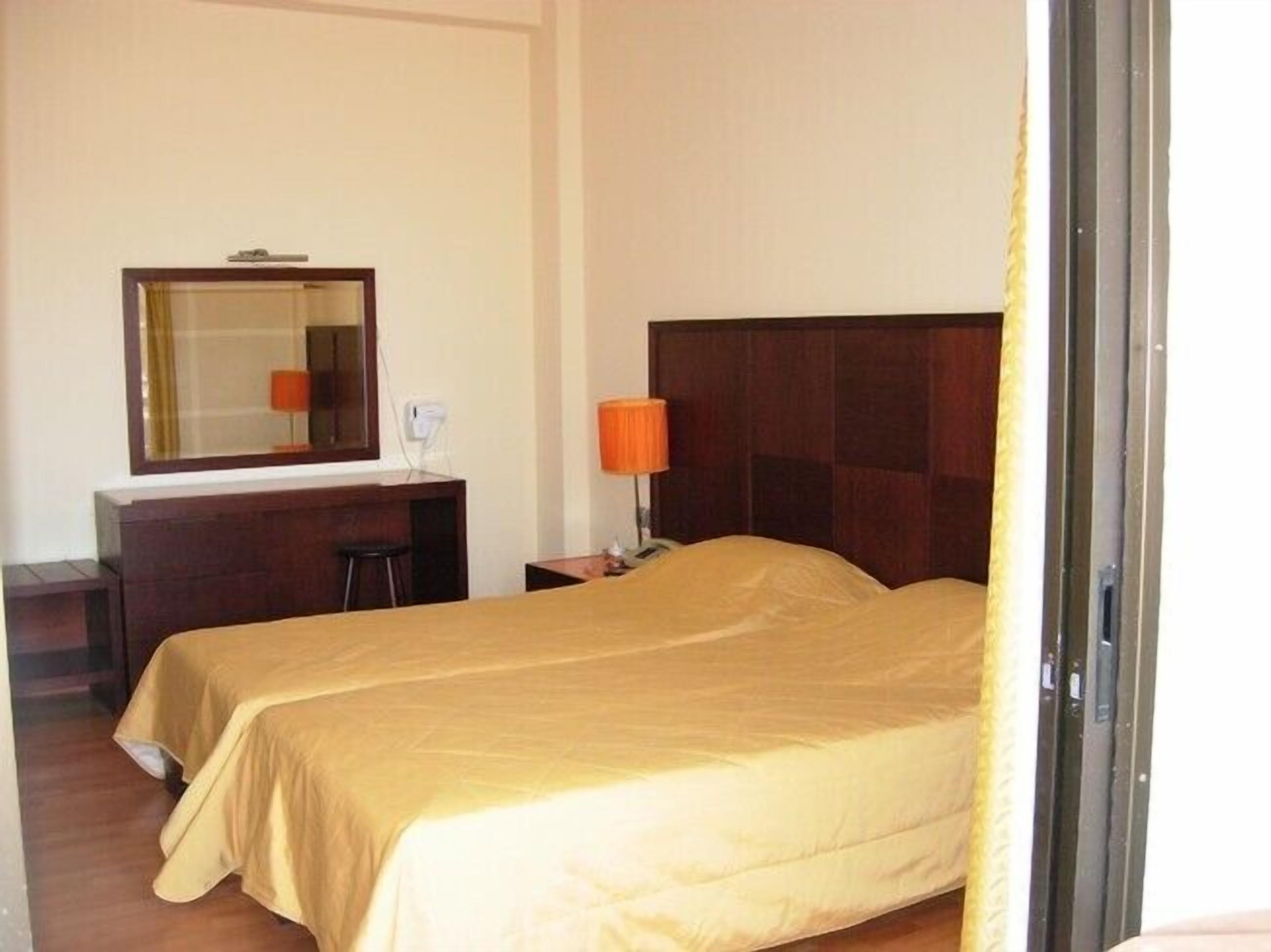 A hotel room with two beds, a desk, a chair, a lamp, and a mirror.