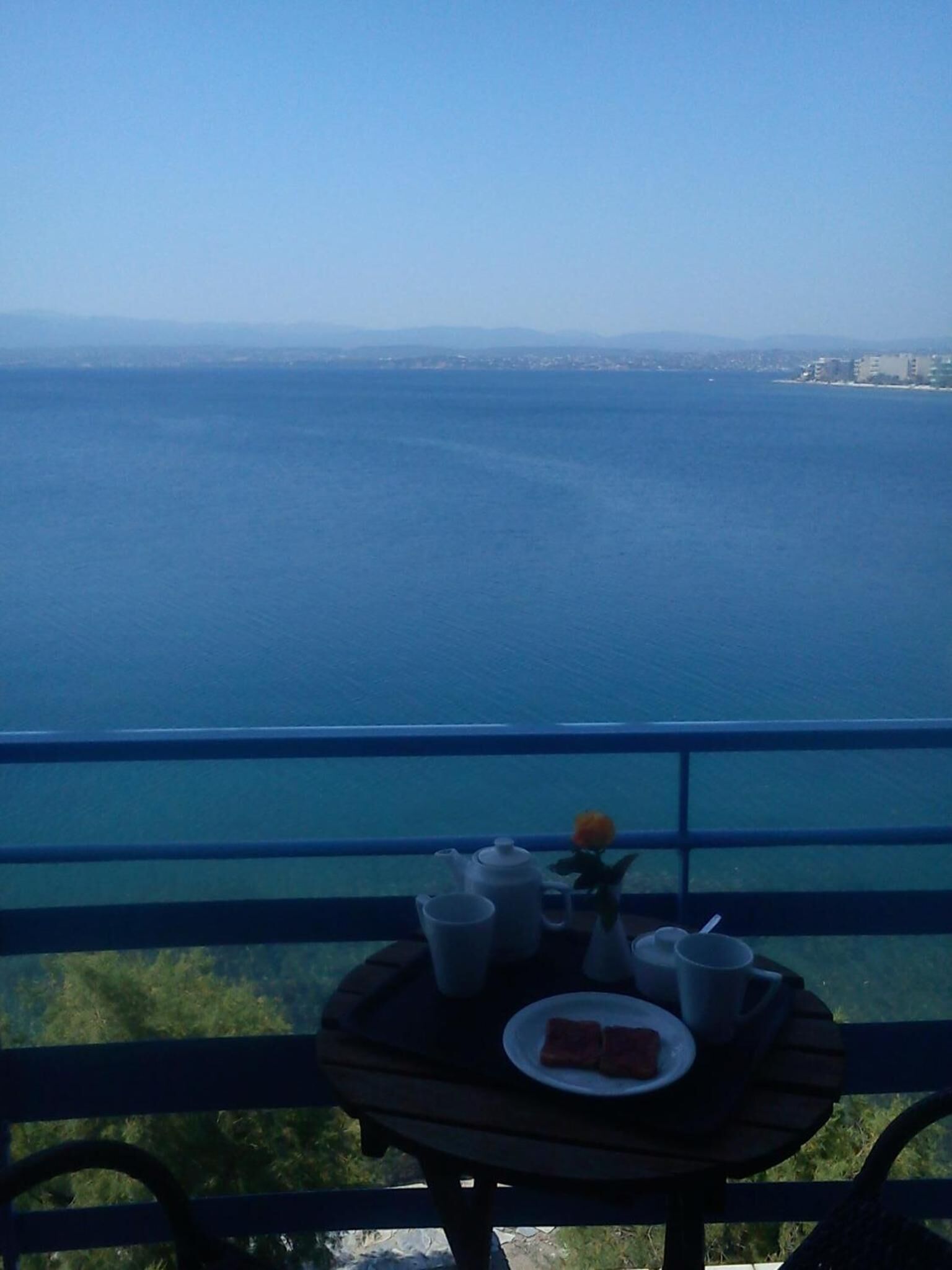 A table with a tray of food and drinks on a balcony overlooking a large body of water.