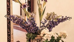 Una mesa redonda de madera con un espejo, jarrones y una campana de cristal con flores.