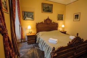Habitación de hotel con una cama grande, dos mesitas de noche con lámparas, un cabecero de madera y tres cuadros enmarcados en las paredes.