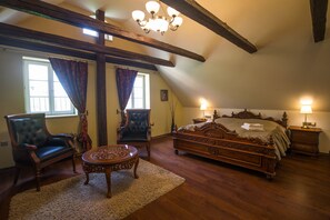 Un dormitorio con una cama grande, dos sillones, una mesita y una araña.