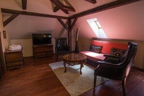 A cozy loft-style room with a wooden floor, a television, a sofa with red cushions, a black leather armchair, and a small round table. - Depandance Edward Kelly (Cesky Krumlov)