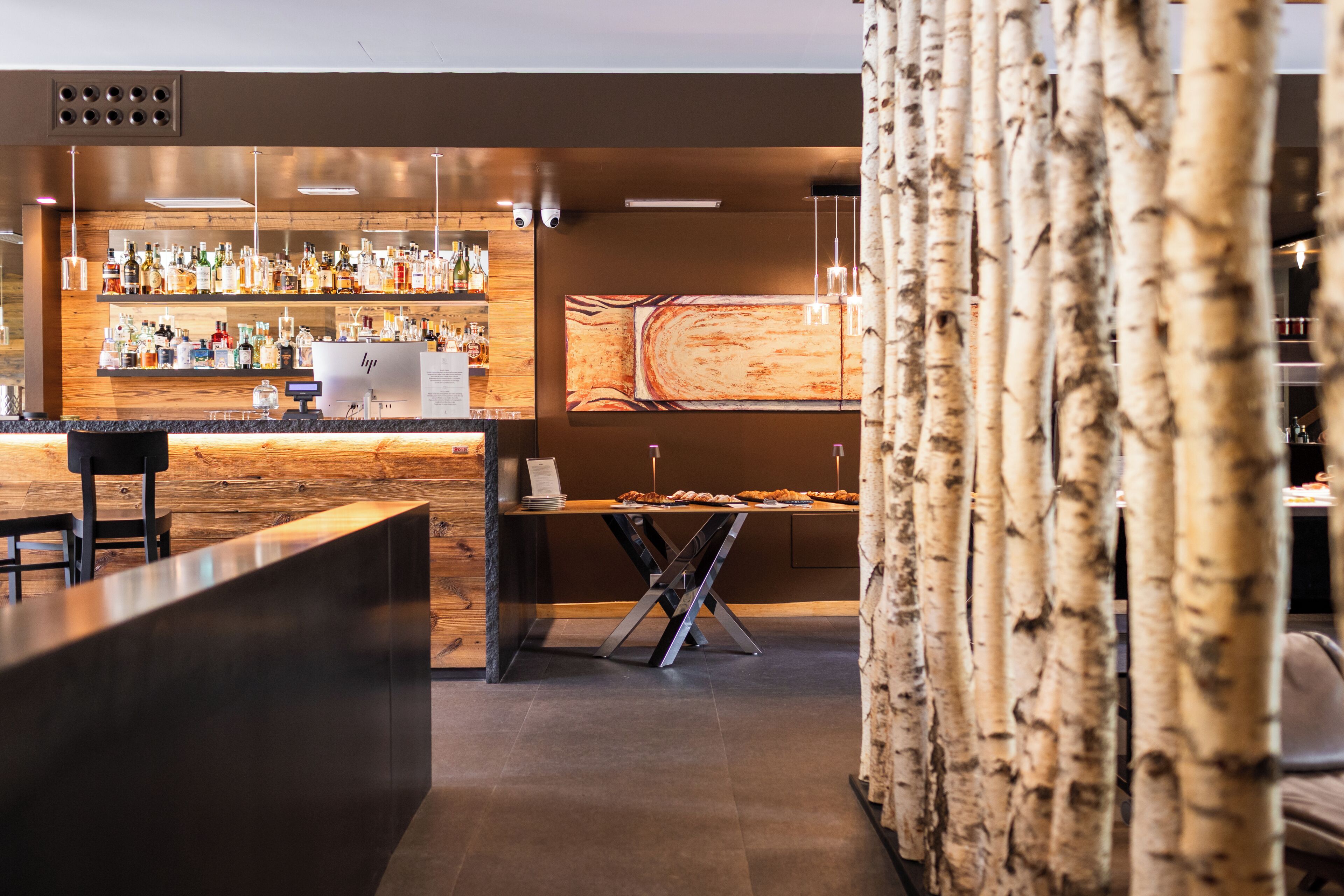 A bar area with a wooden counter, shelves of liquor bottles, and a seating area with a table and chairs.