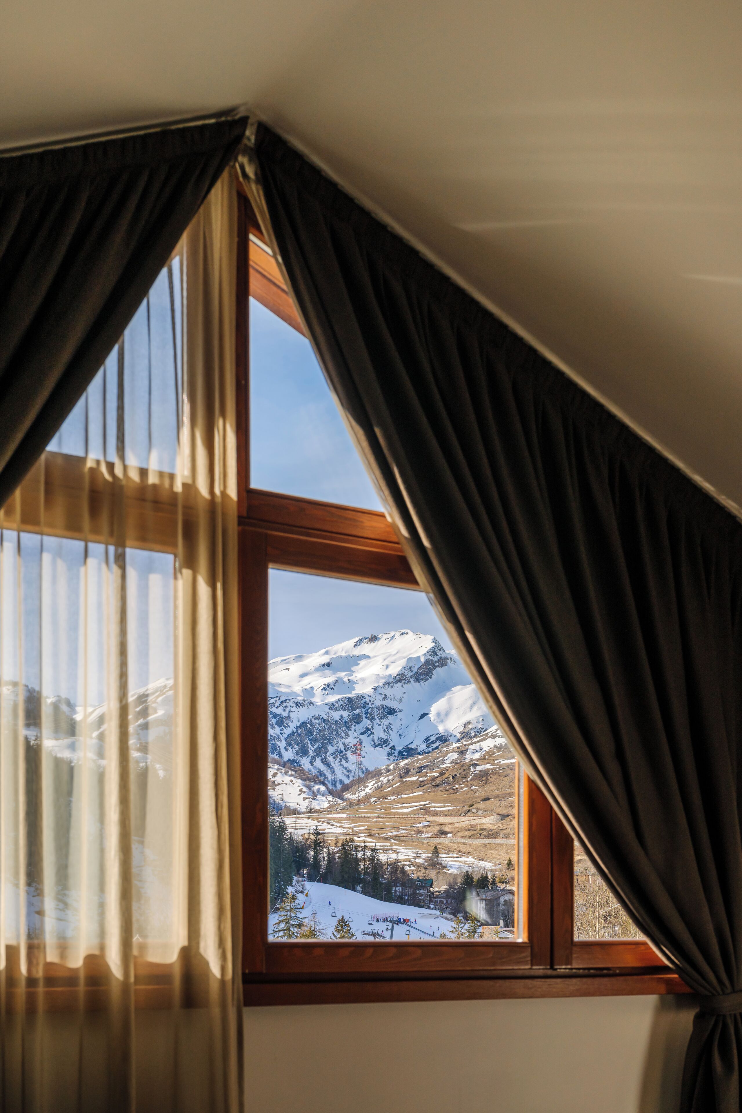 Una ventana con cortinas que muestra un paisaje nevado de montañas.