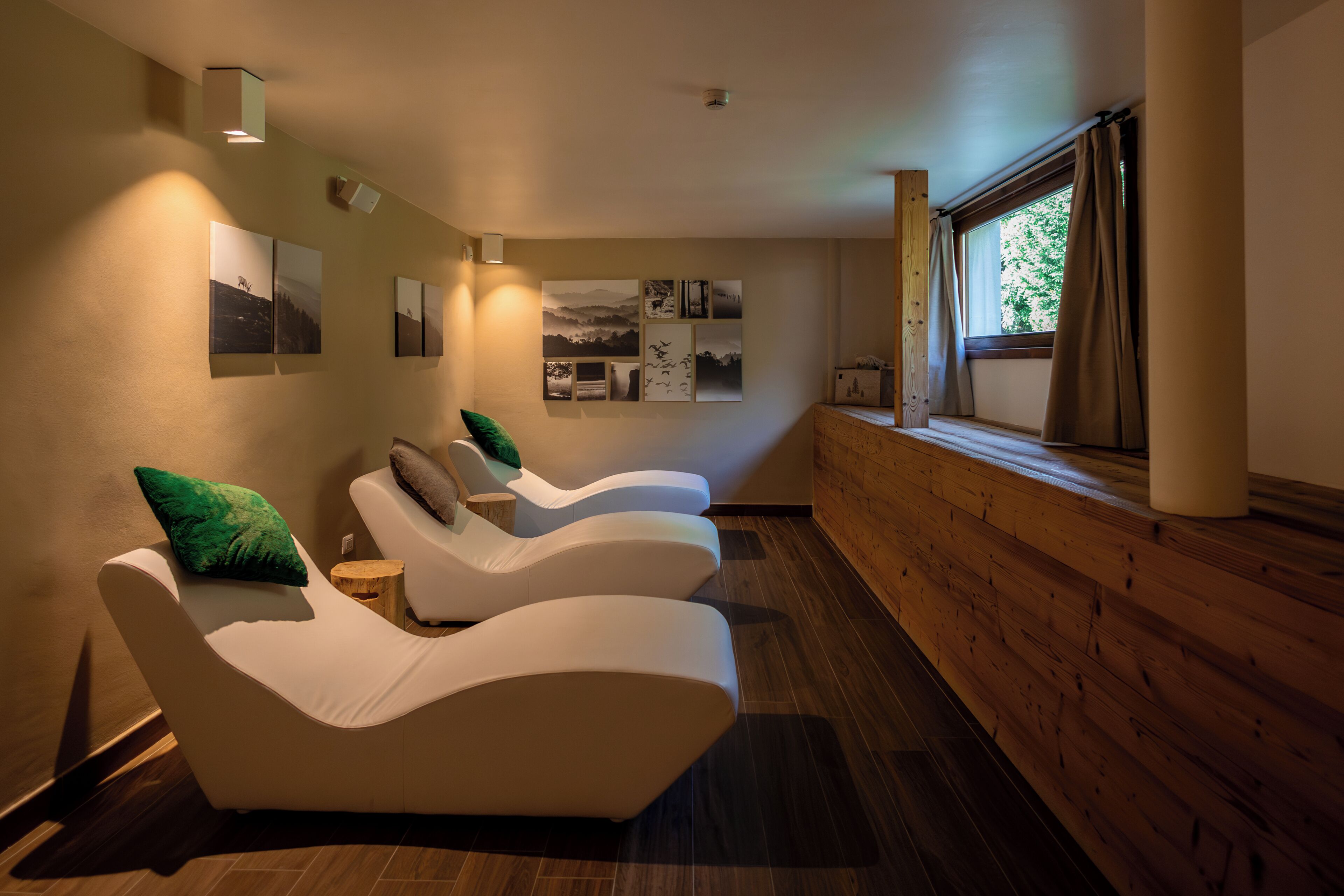 Un cuarto de spa con tres sillas reclinables, suelo de madera y obras de arte colgadas en la pared.