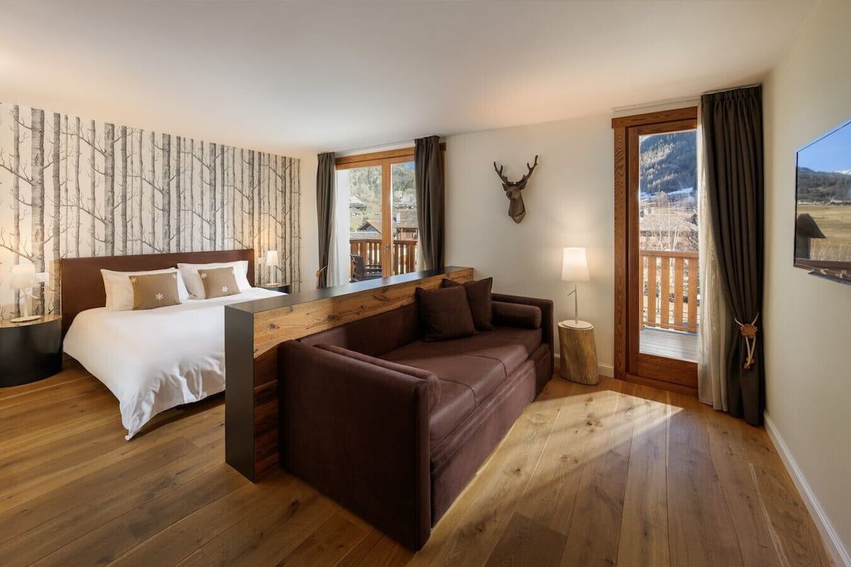 A bedroom with a bed, a brown sofa, a wooden bench, and a deer head decoration.