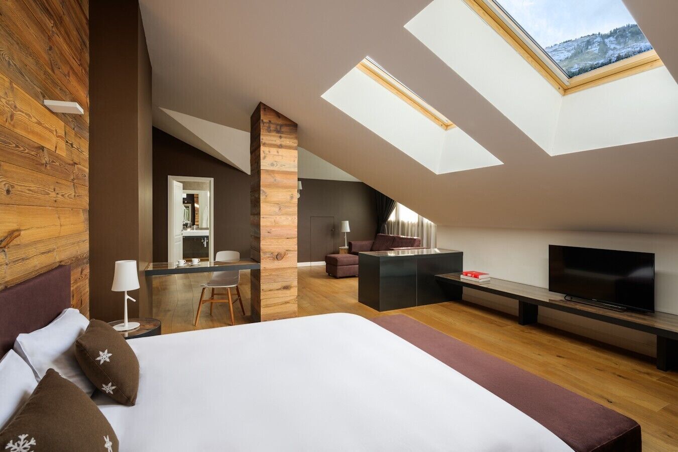 A modern loft bedroom with a skylight, a TV, and a cozy seating area.
