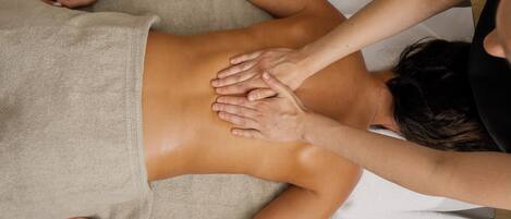 A person receiving a back massage on a massage table with a towel covering their lower body.