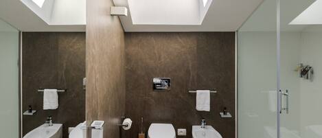 A modern bathroom with skylights, a large bathtub, two sinks, and a glass-enclosed shower.