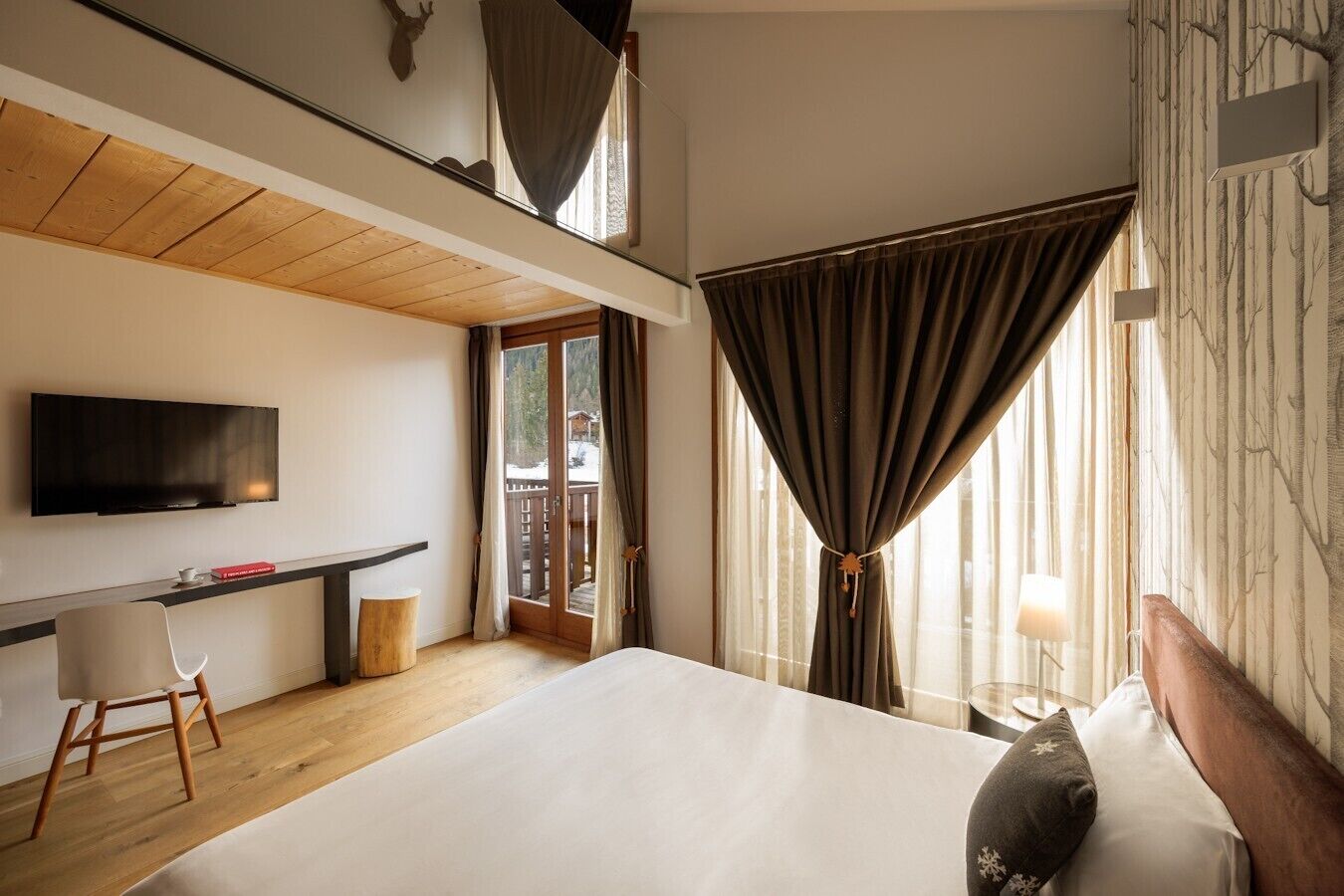 A modern hotel room with a large bed, a desk, a television, and a view of the outdoors.