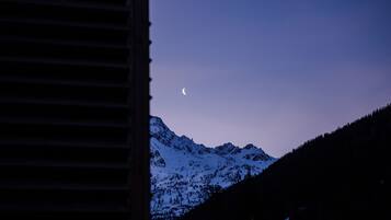 Catena montuosa con una luna crescente nel cielo, vista da una finestra con persiane orizzontali.
