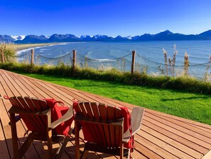 A wooden deck with two red Adirondack chairs facing a lake with mountains in the background.
