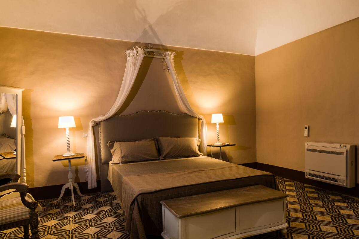 Een slaapkamer met een hemelbed, bedlampen, een spiegel en een vloer met een patroon.